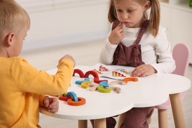 Photo of Little children playing with colorful wooden pieces at white table indoors. Developmental toy