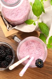 Different glassware of delicious blackberry smoothie and fresh berries on wooden table, flat lay