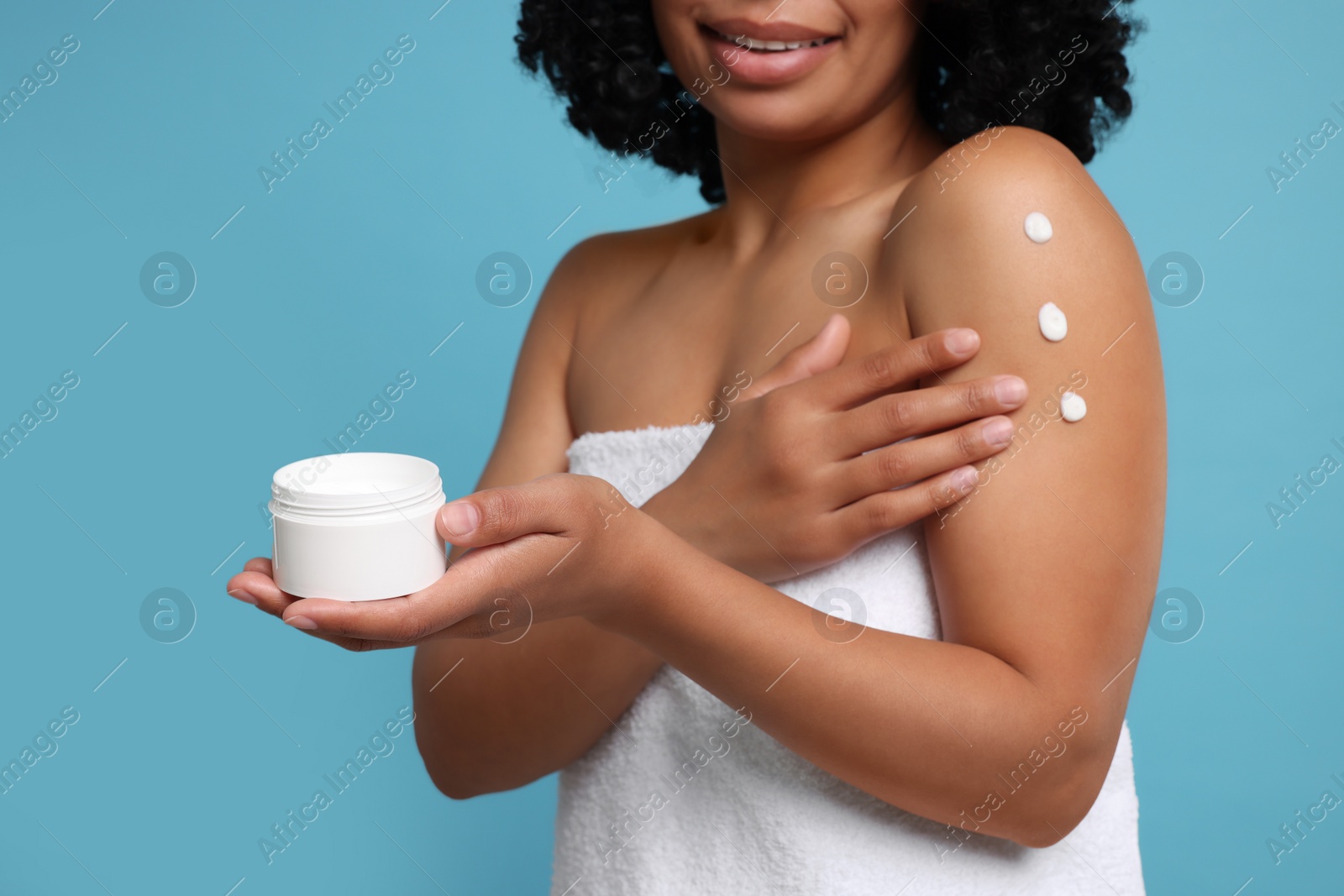 Photo of Young woman applying body cream onto shoulder on light blue background, closeup