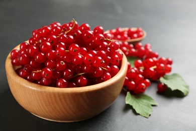 Photo of Ripe red currants in wooden bowl on black table
