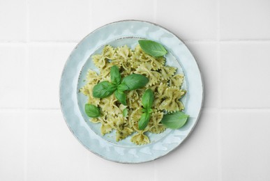 Photo of Delicious pasta with pesto sauce and basil on white tiled table, top view
