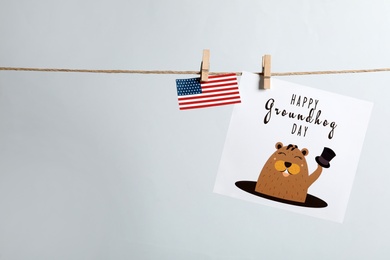 Photo of Happy Groundhog Day greeting card and American flag hanging on light background, space for text