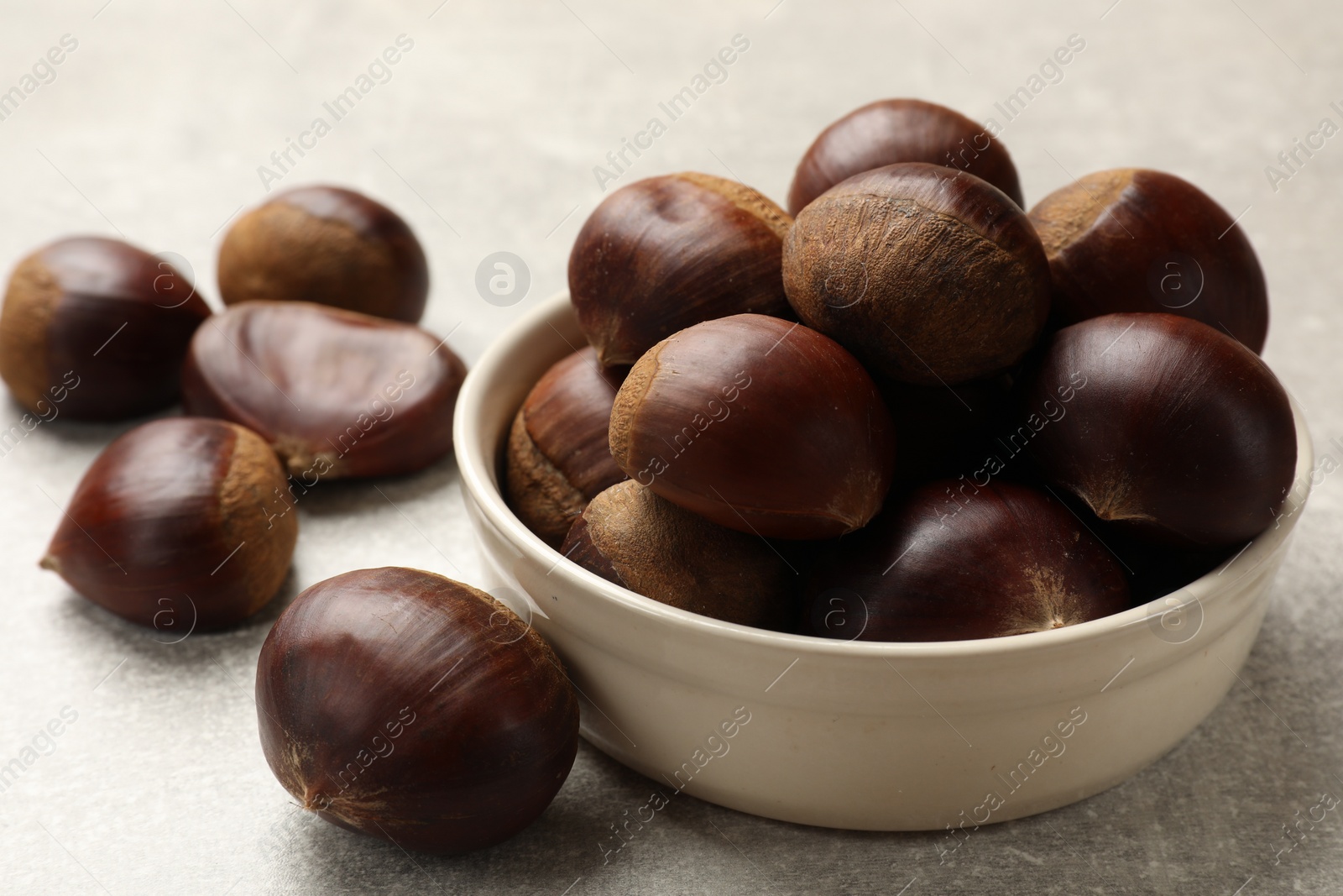 Photo of Bowl with roasted edible sweet chestnuts on light grey table, closeup