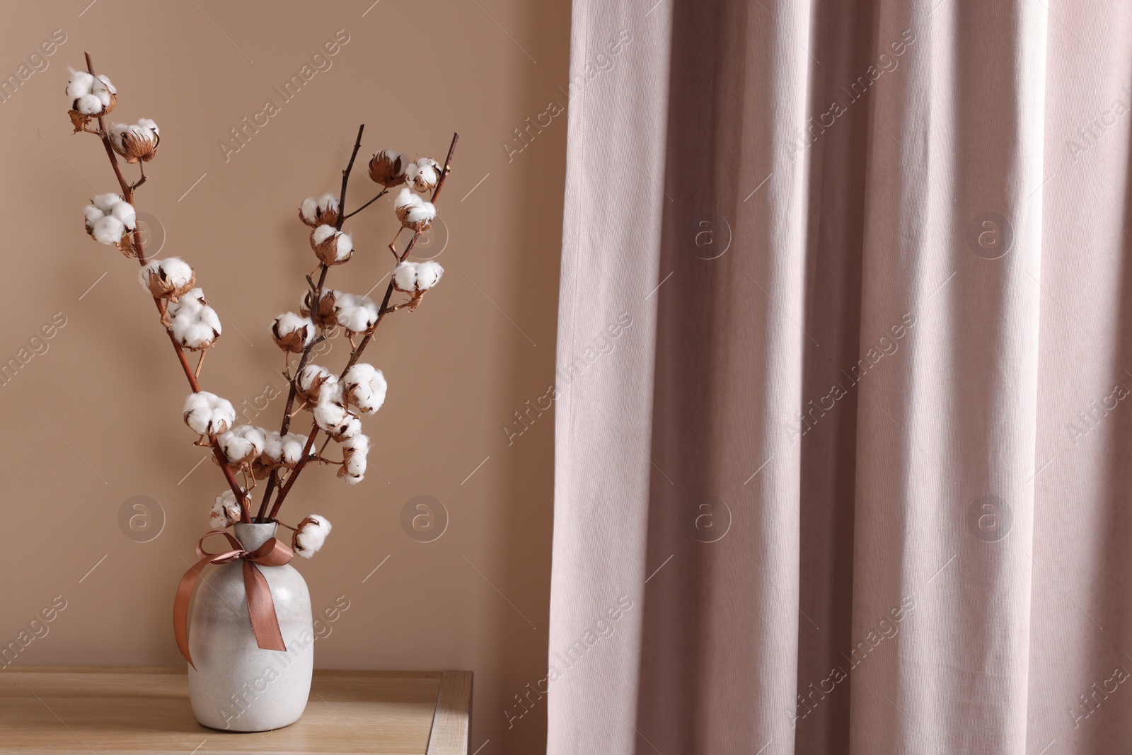 Photo of Vase with beautiful bouquet of white fluffy cotton flowers on wooden table in cozy room