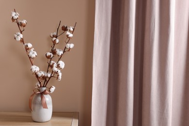 Photo of Vase with beautiful bouquet of white fluffy cotton flowers on wooden table in cozy room