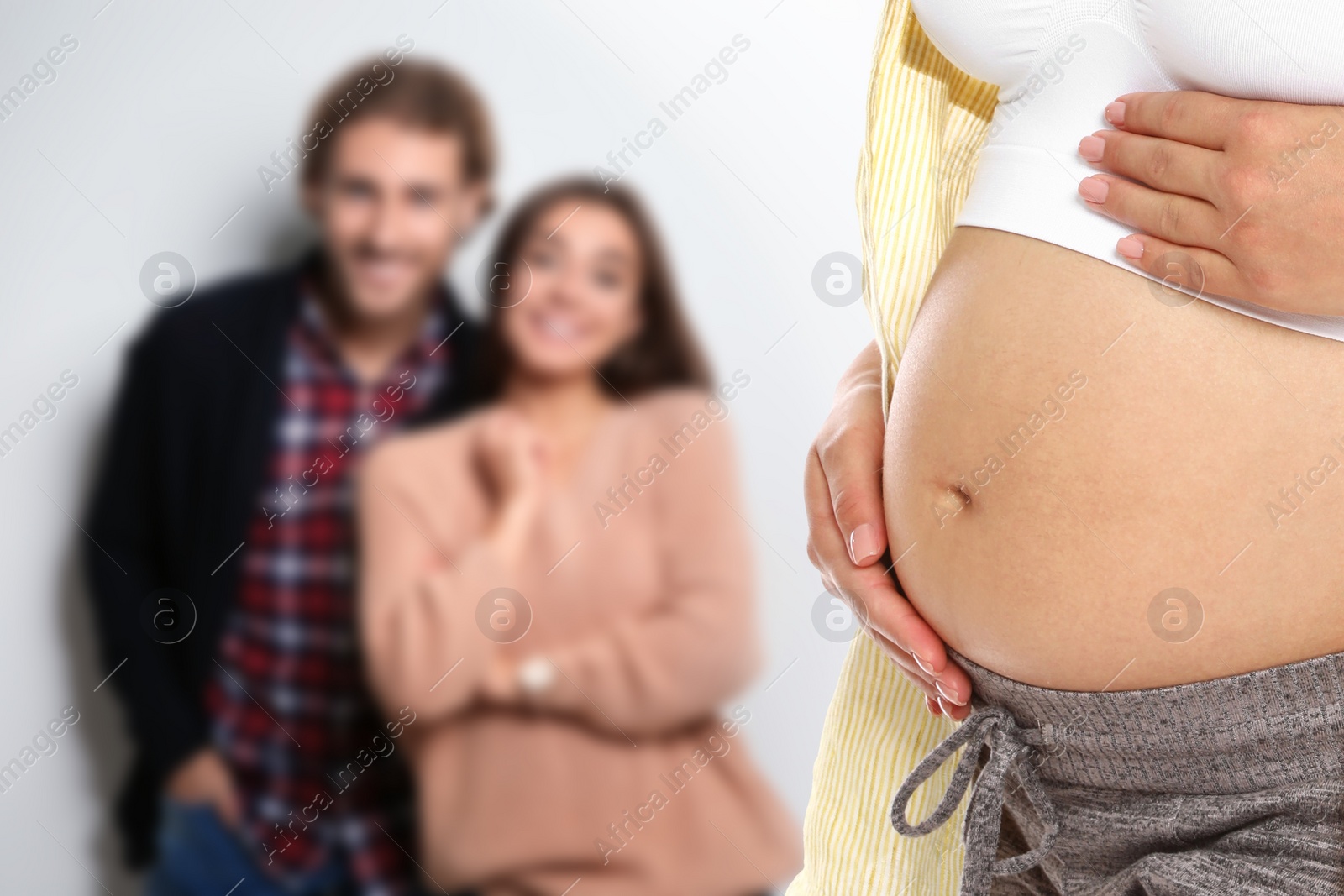 Image of Surrogacy concept. Young pregnant woman and blurred view of happy couple on light background