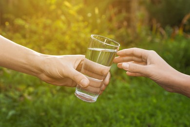 Photo of Man giving glass of fresh water to woman outdoors, closeup