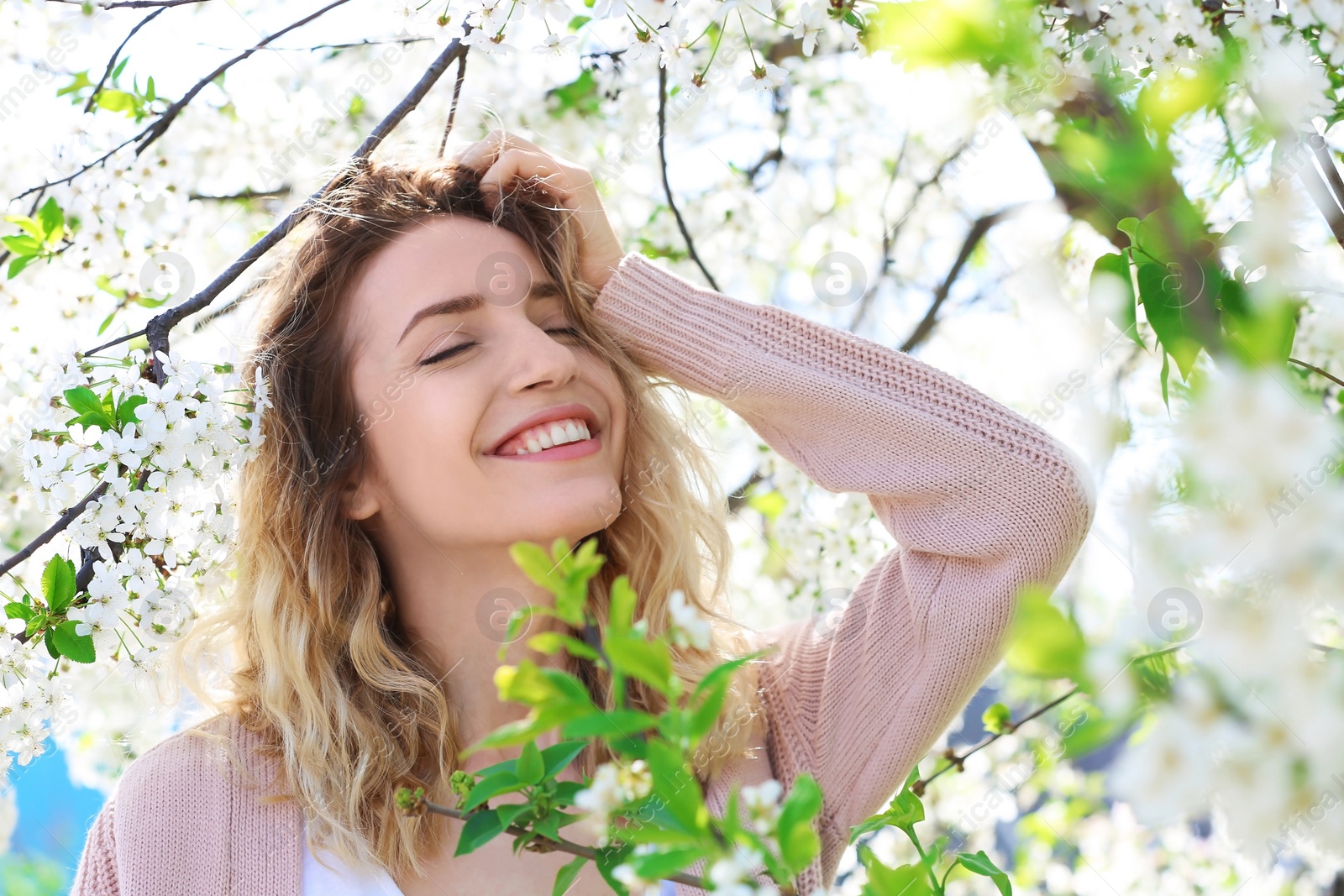 Photo of Attractive young woman posing near blossoming tree on sunny spring day