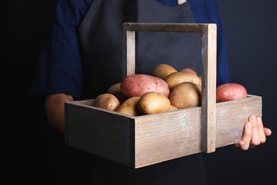 Photo of Person holding wooden basket with fresh organic potatoes on black background