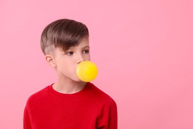 Photo of Boy blowing bubble gum on pink background, space for text
