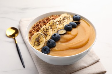 Photo of Delicious smoothie bowl with fresh blueberries, banana and granola on white table, closeup