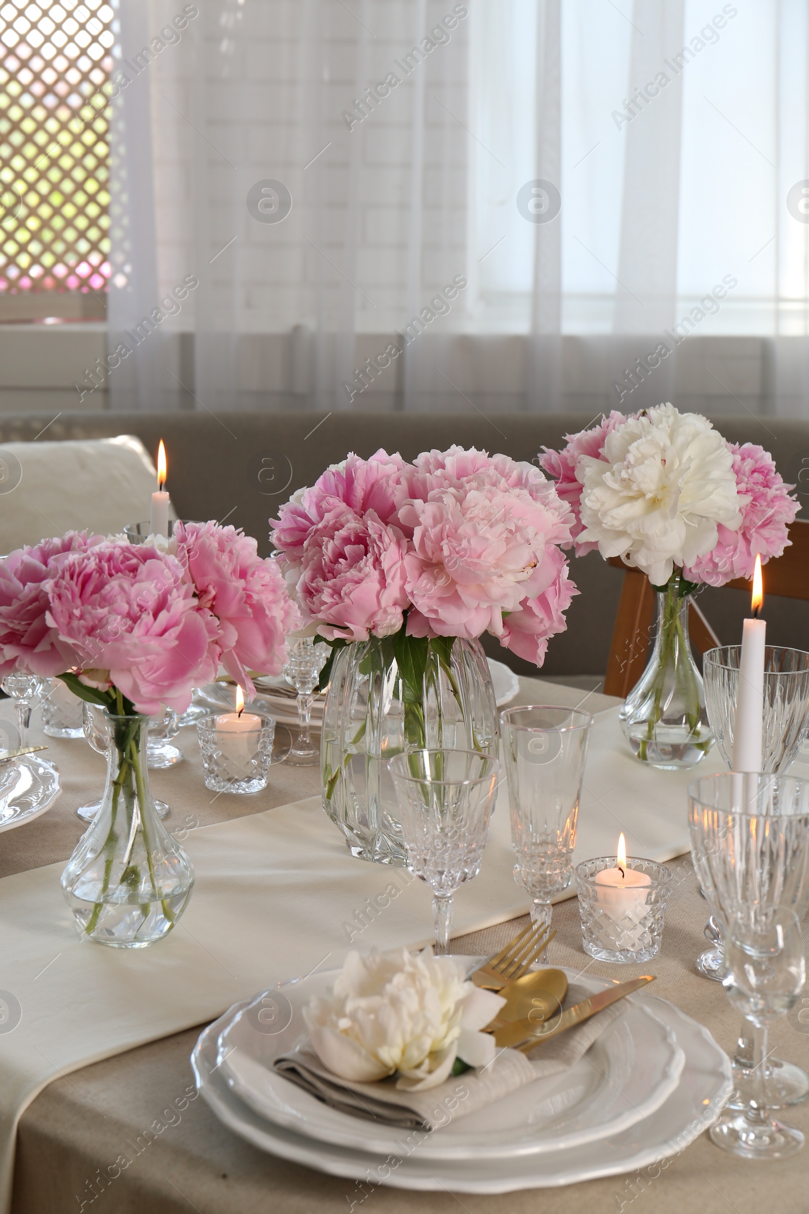 Photo of Stylish table setting with beautiful peonies and burning candles indoors