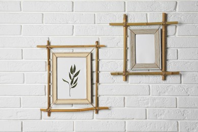 Photo of Stylish bamboo frames hanging on white brick wall
