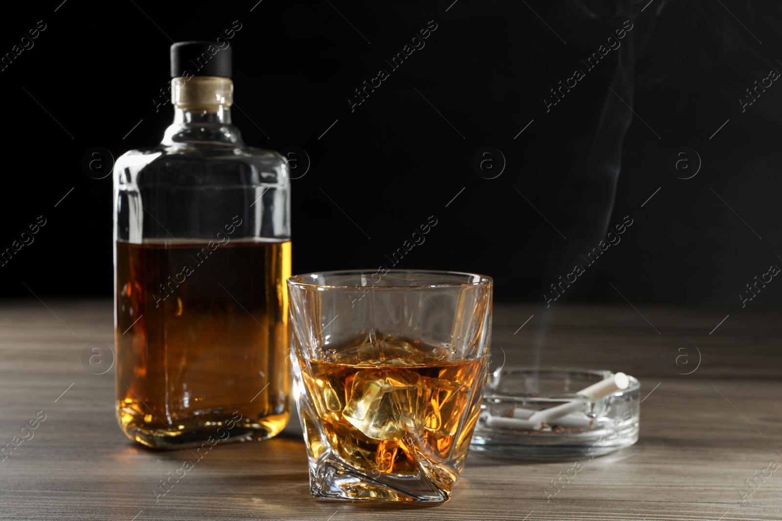 Photo of Alcohol addiction. Whiskey in glass, bottle, cigarettes and ashtray on wooden table