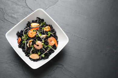 Photo of Delicious black risotto with seafood in bowl on grey table, top view. Space for text