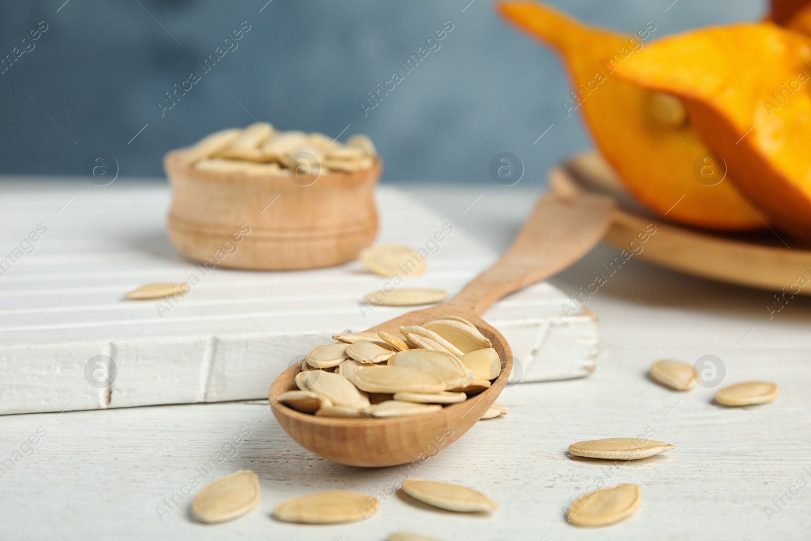 Photo of Spoon of raw pumpkin seeds on white wooden table