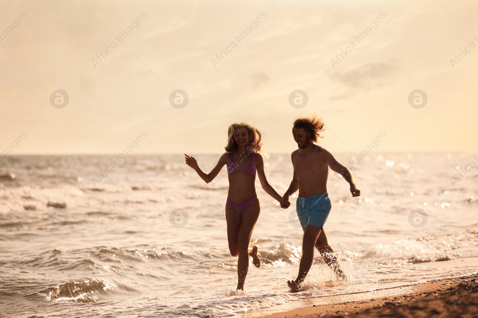 Photo of Young woman in bikini and her boyfriend having fun on beach at sunset. Lovely couple