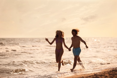 Young woman in bikini and her boyfriend having fun on beach at sunset. Lovely couple