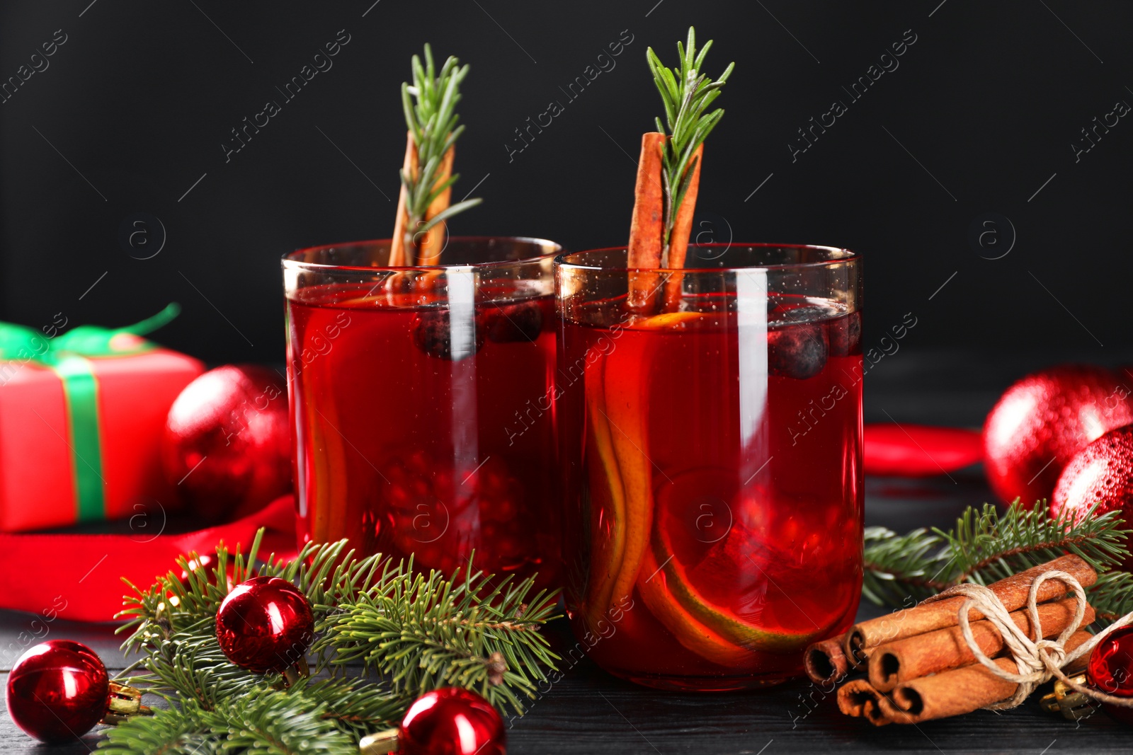 Photo of Aromatic Sangria drink in glasses, ingredients and Christmas decor on black wooden table