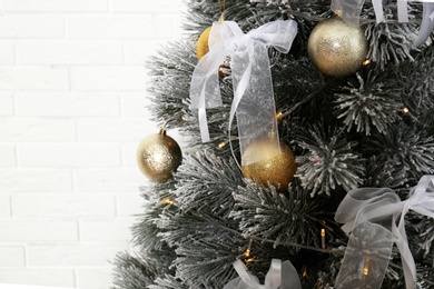 Decorated Christmas tree near white brick wall, closeup