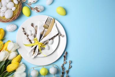Photo of Festive table setting with tulips and painted eggs on light blue background, flat lay with space for text. Easter celebration