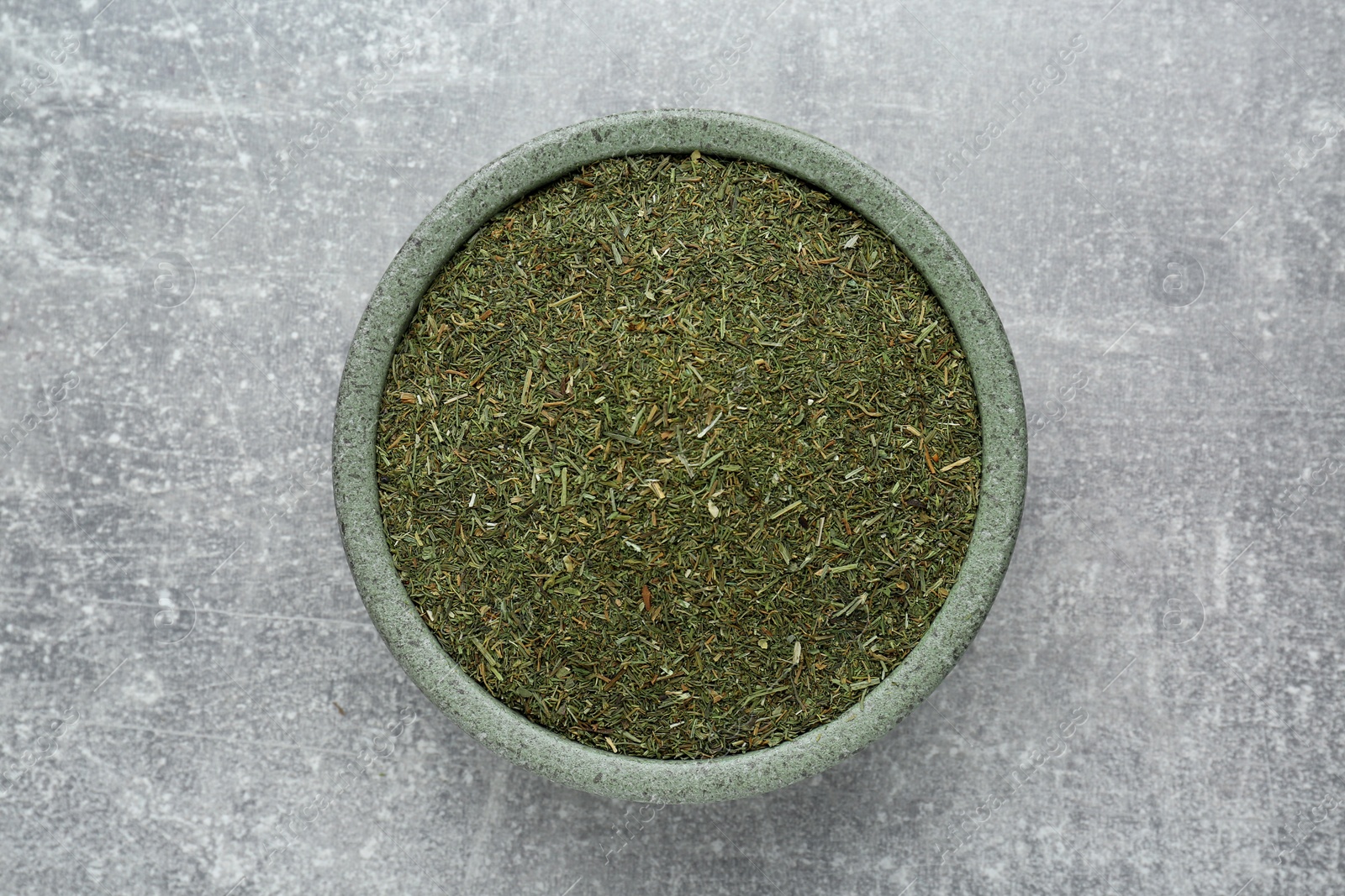 Photo of Dried dill in bowl on light grey table, top view