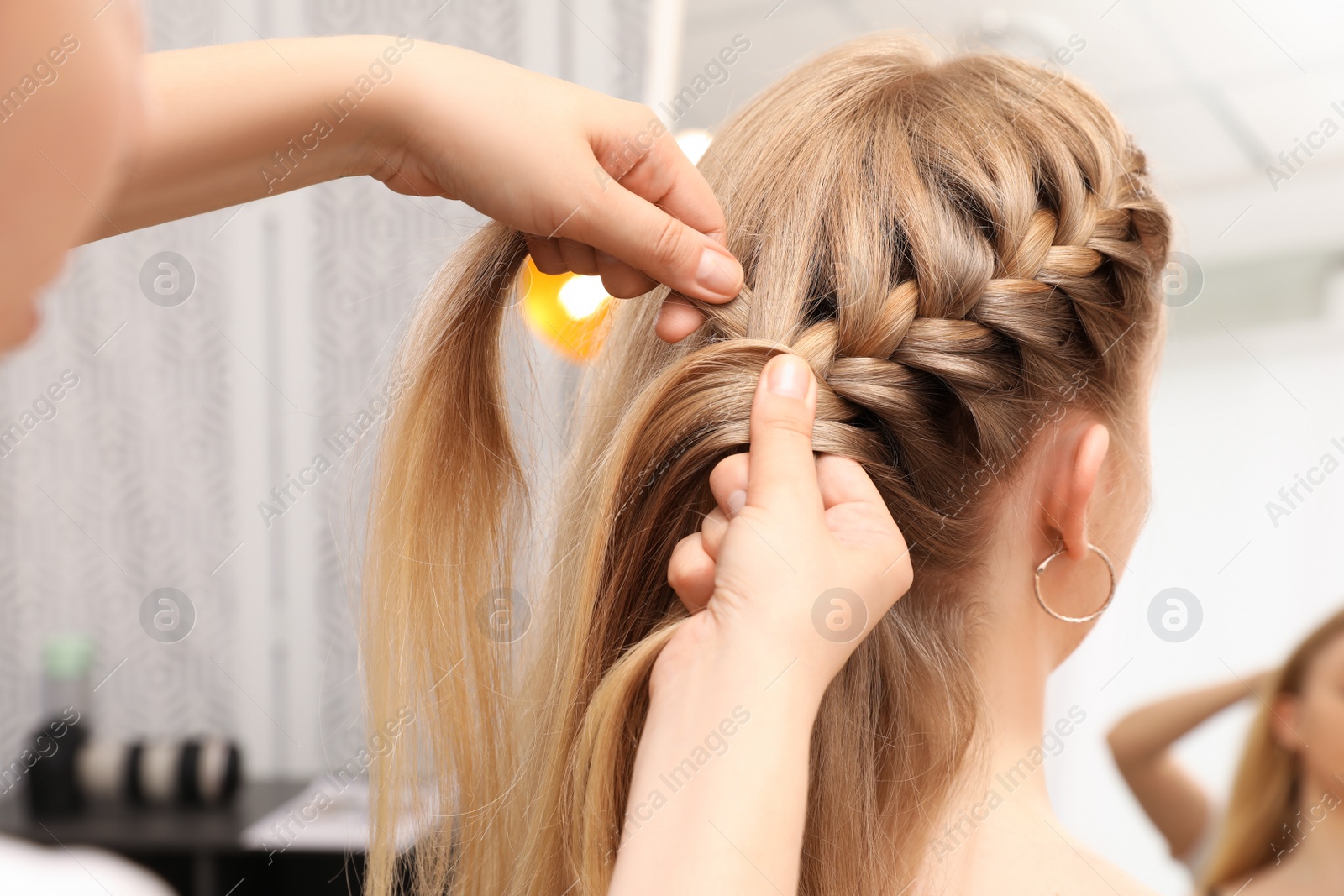 Photo of Professional stylist braiding client's hair in salon