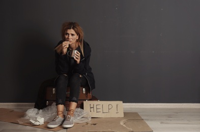 Photo of Poor homeless woman with bread and mug asking for help near dark wall. Space for text