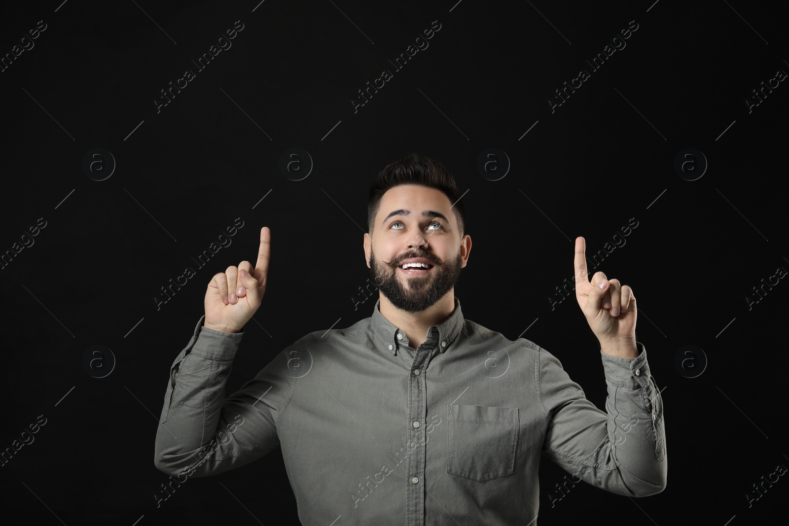 Photo of Young man with mustache pointing at something on black background. Space for text