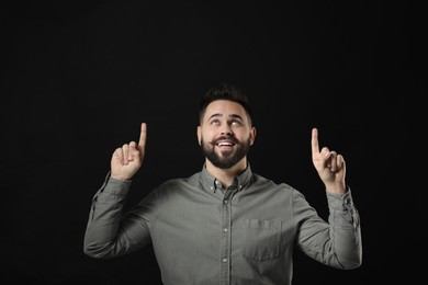 Young man with mustache pointing at something on black background. Space for text