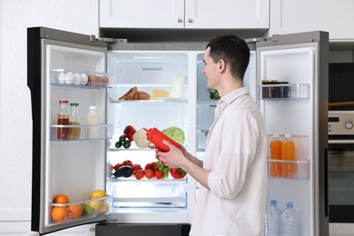 Photo of Happy man holding ketchup near refrigerator in kitchen