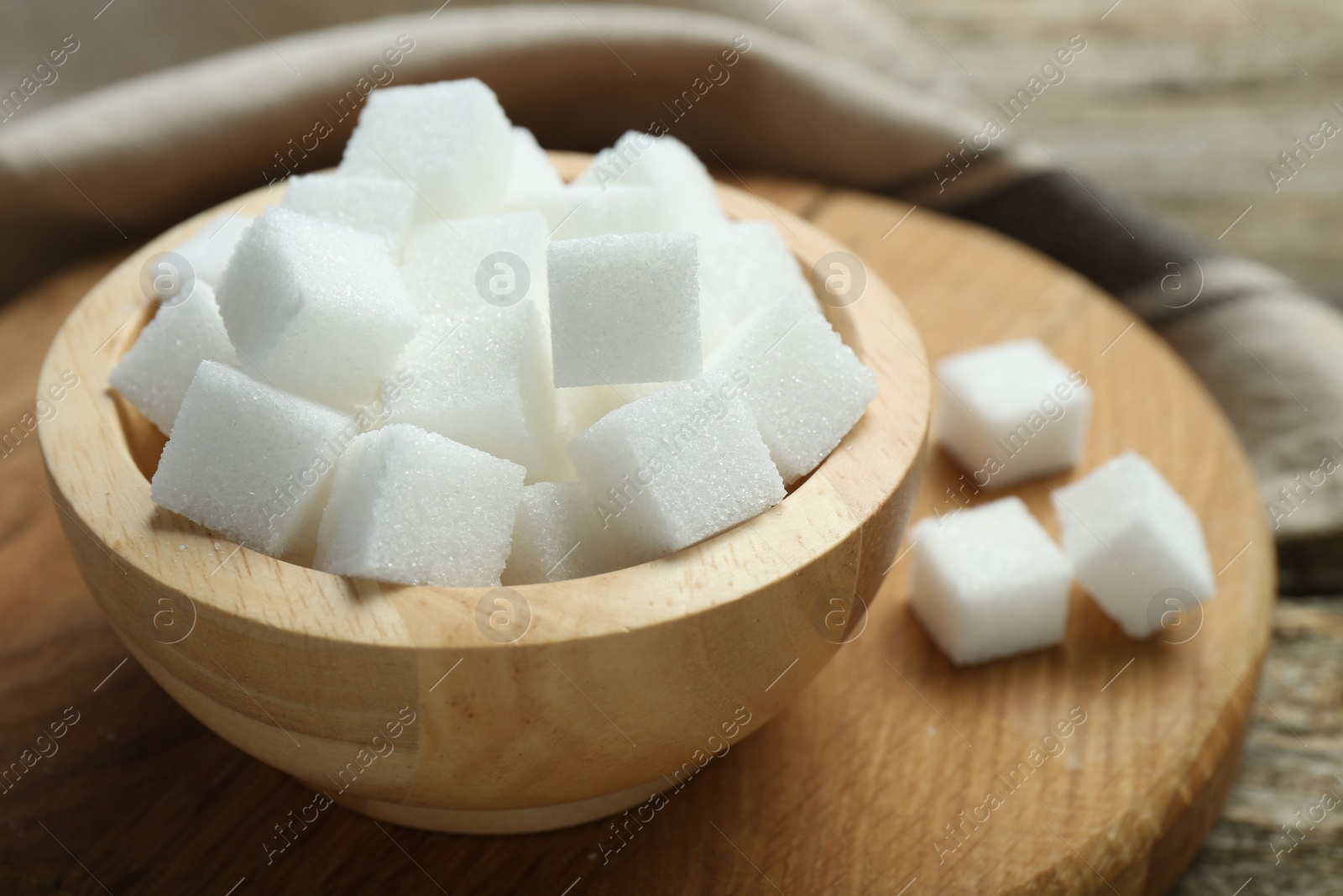 Photo of White sugar cubes in bowl on wooden board, closeup