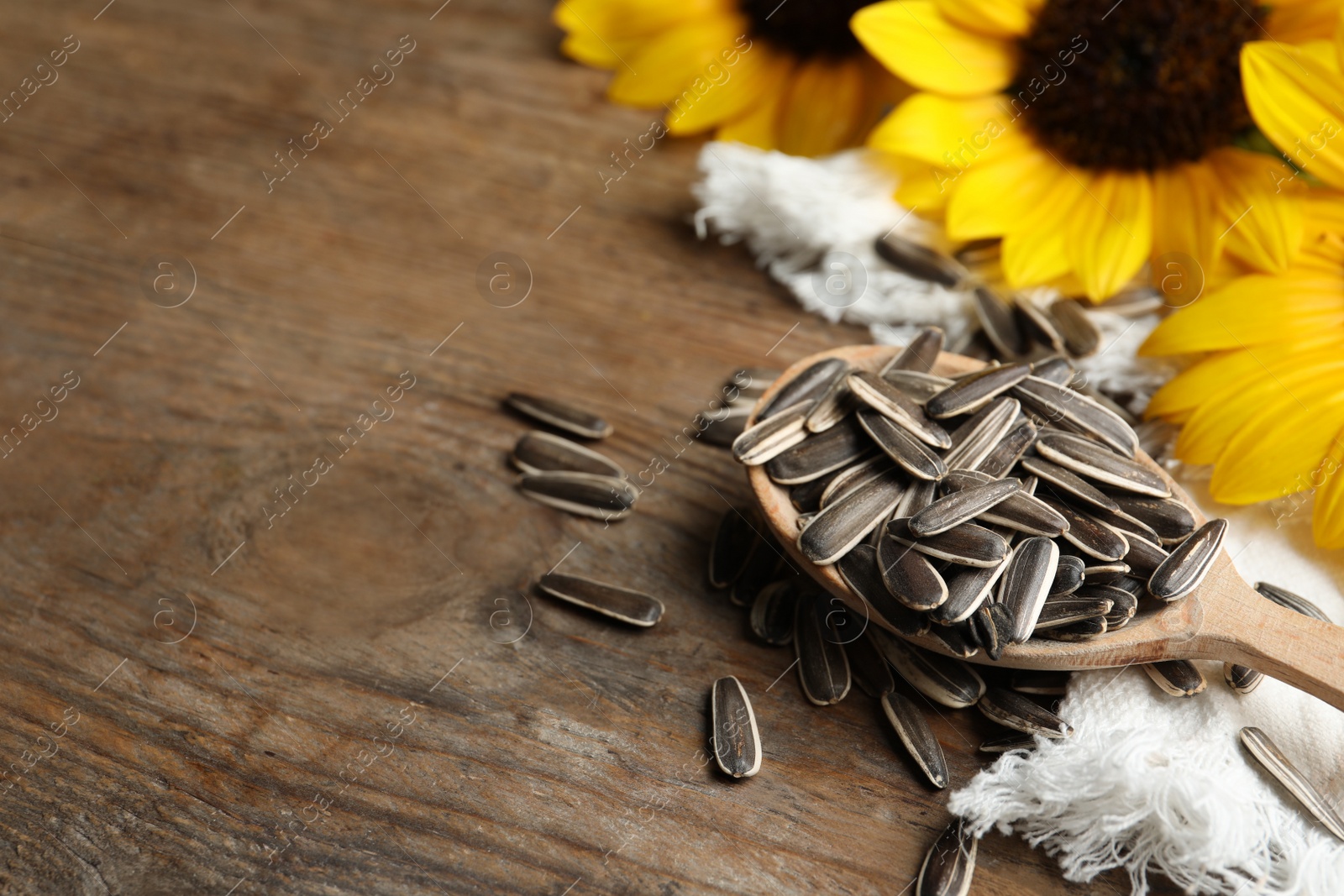 Photo of Organic sunflower seeds and flowers on wooden table, closeup. Space for text