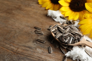 Photo of Organic sunflower seeds and flowers on wooden table, closeup. Space for text