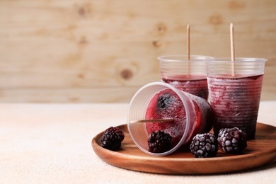 Photo of Tasty blackberry ice pops in plastic cups on white table, space for text. Fruit popsicle