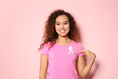 Photo of African-American woman with silk ribbon on color background. Breast cancer awareness concept