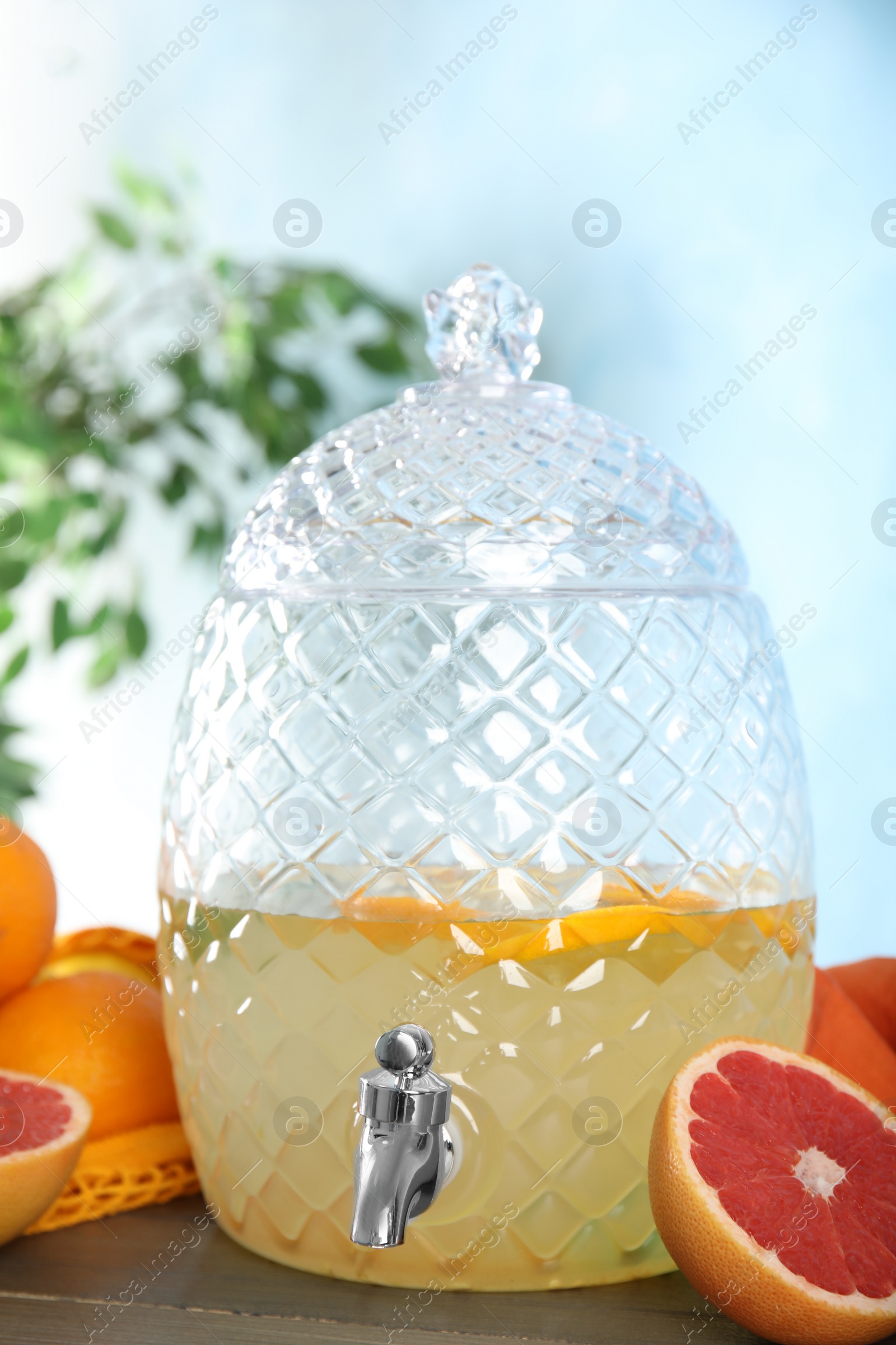 Photo of Delicious refreshing lemonade in glass dispenser and fruits on wooden table