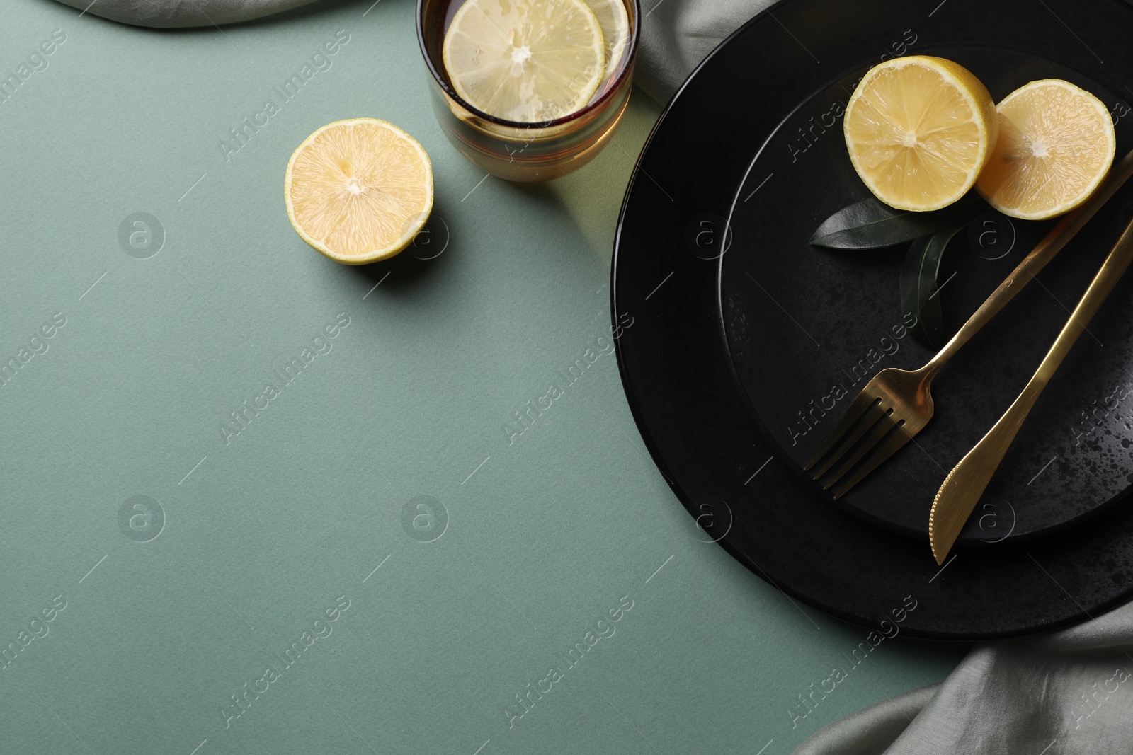 Photo of Stylish table setting. Plates, cutlery and tea with lemon on olive background, top view. Space for text