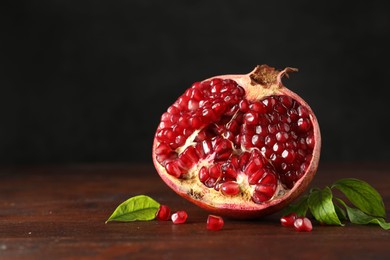 Photo of Cut fresh pomegranate and green leaves on wooden table, space for text