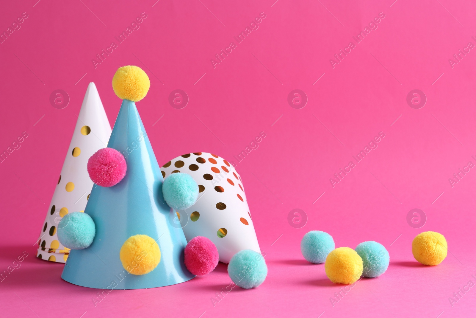 Photo of Party hats with color pompoms on pink background