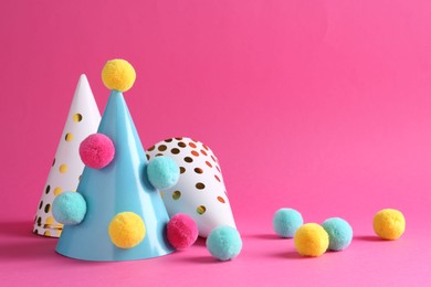Photo of Party hats with color pompoms on pink background