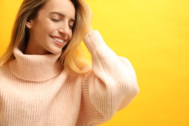 Beautiful young woman wearing knitted sweater on yellow background. Space for text
