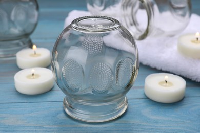 Photo of Glass cups and burning candles on light blue wooden table, closeup. Cupping therapy