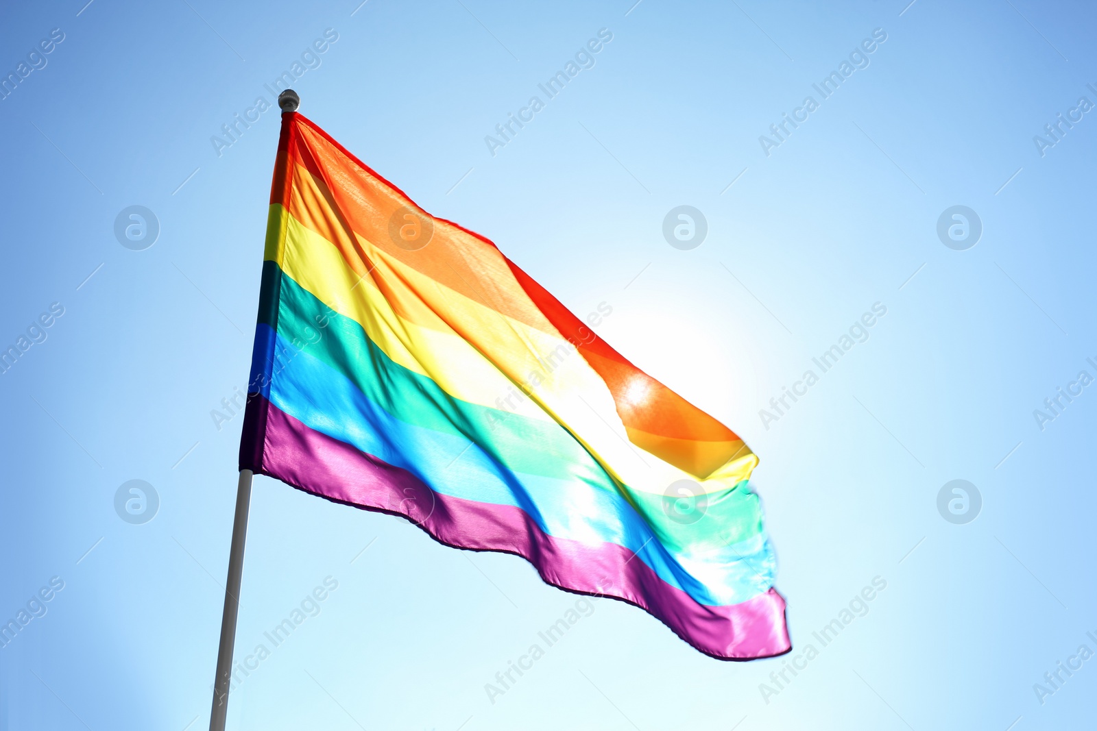 Photo of Rainbow LGBT flag fluttering on blue sky background. Gay rights movement