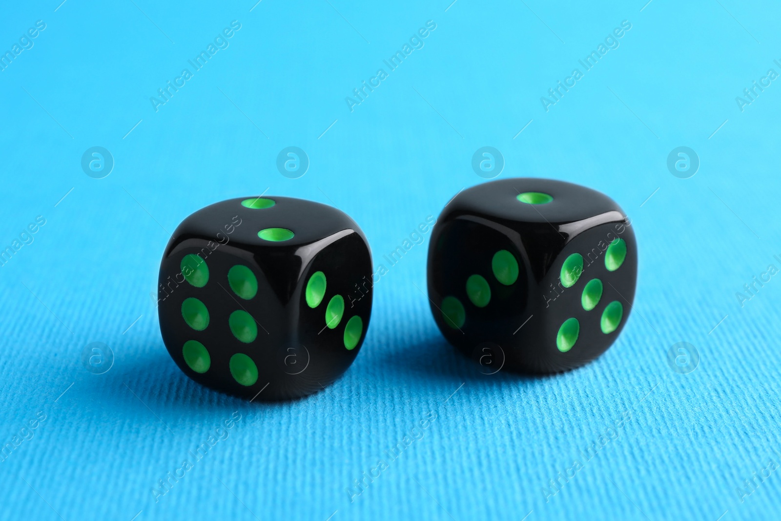 Photo of Two black game dices on light blue background, closeup