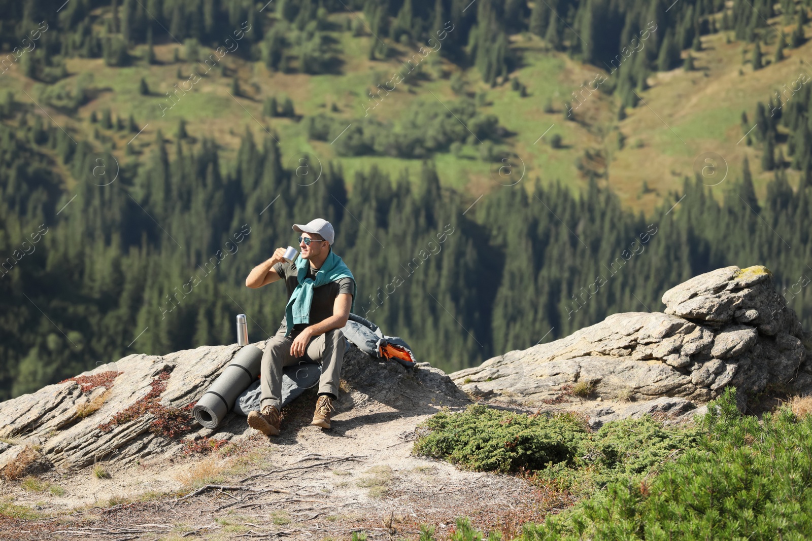 Photo of Tourist with hot drink, sleeping bag and mat on mountain peak