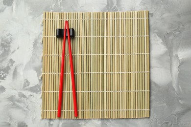 Bamboo mat with pair of red chopsticks and rest on grey textured table, top view