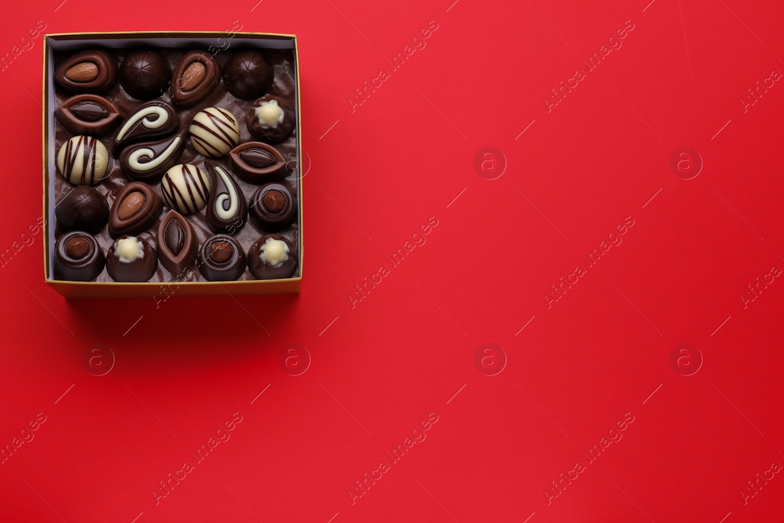 Photo of Box of delicious chocolate candies on red background, top view. Space for text