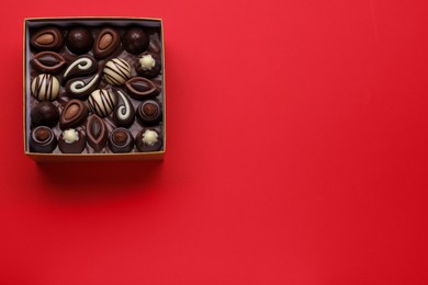 Box of delicious chocolate candies on red background, top view. Space for text