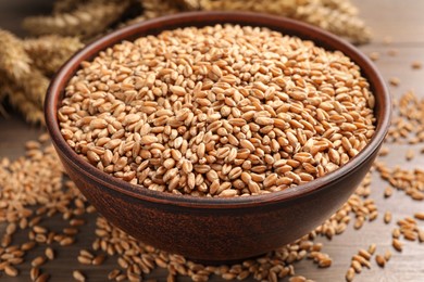 Photo of Wheat grains in bowl on wooden table, closeup